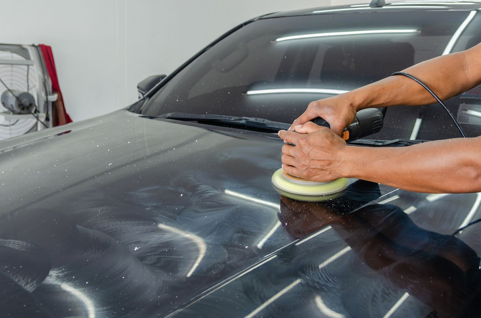 Hands using a machine polisher on a car bonnet